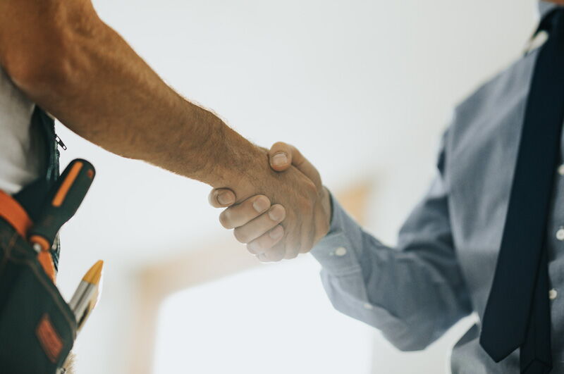 Handwerker gibt Mann mit Anzug und Krawatte die Hand